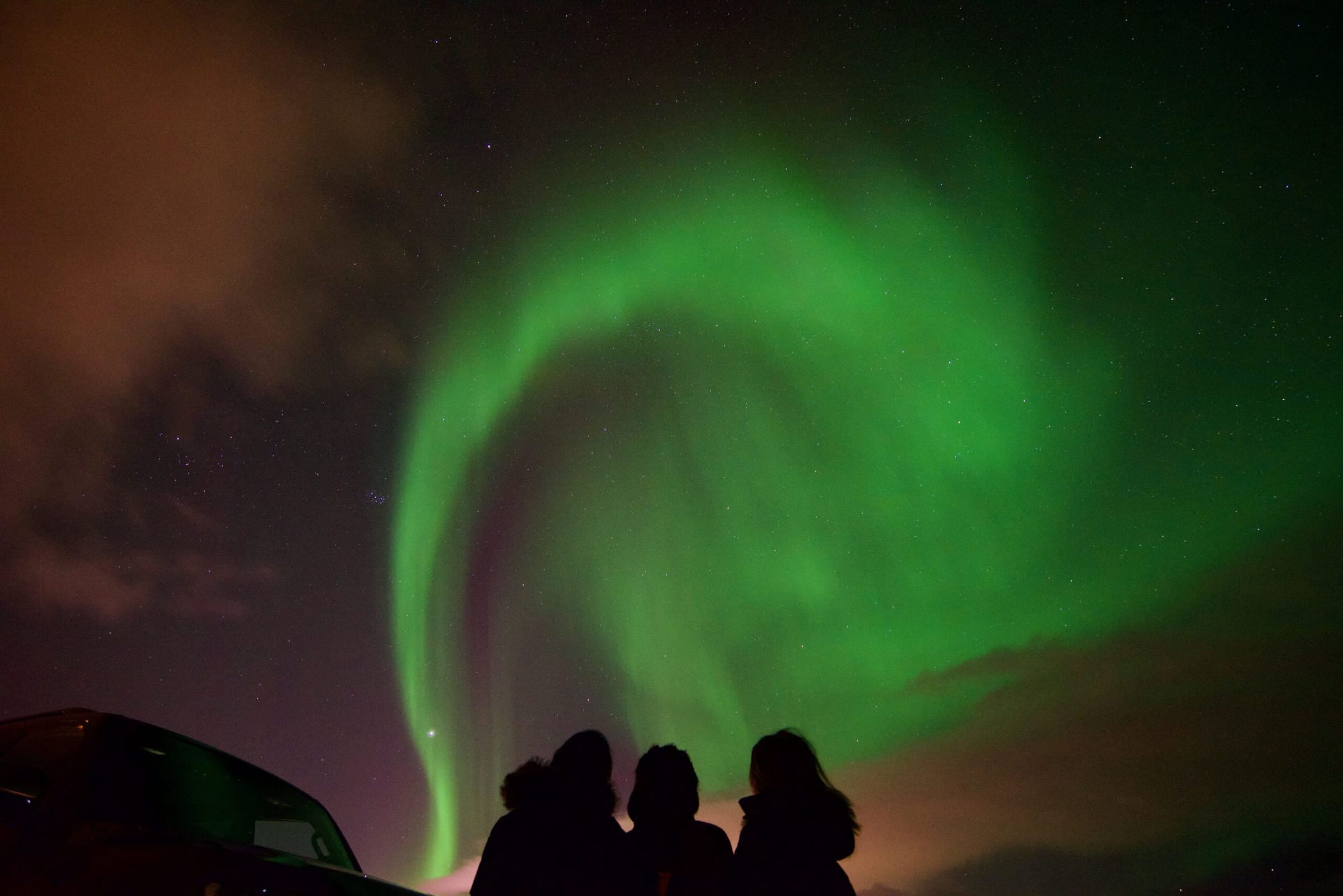 Three travellers silhouetted under a green aurora arc